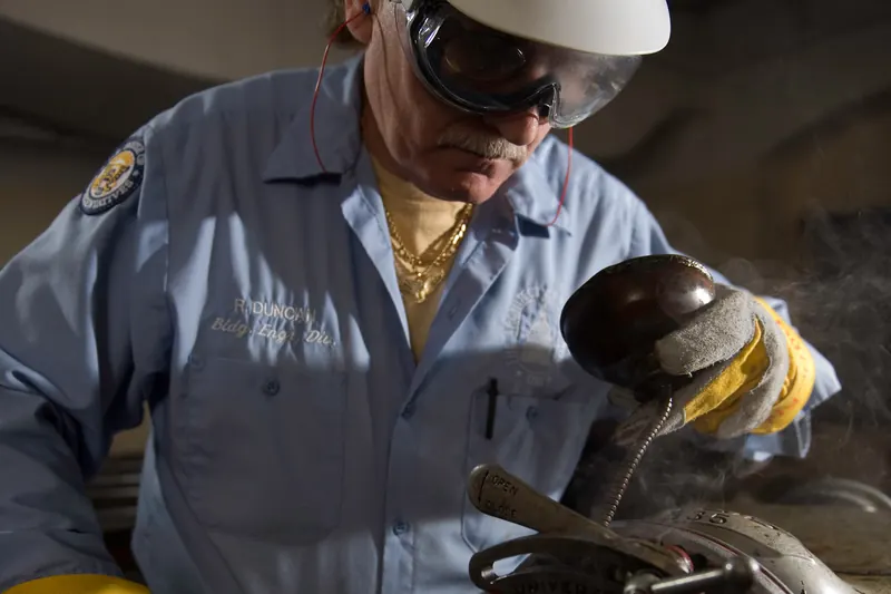 A pipefitter in a hard hat, safety glasses and work gloves working on a valve